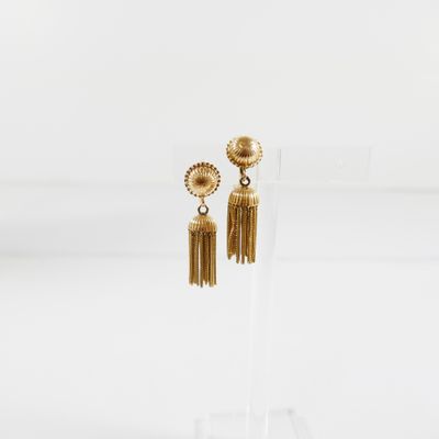 une paire de boucles d'oreilles en or ornées de pompons, présentées sur un support transparent