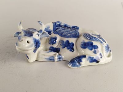 figurine en porcelaine représentant une vache couchée sur une surface blanche