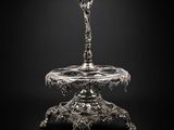 une assiette en argent sur laquelle repose une cuillère, sur fond noir