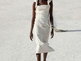une femme qui défile sur un podium, vêtue d'une robe blanche