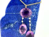 collier avec des pierres violettes et une chaîne en or posé sur une plaque de marbre bleu