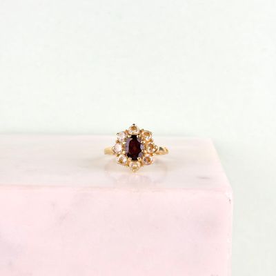 un gros plan d'une bague en or sertie d'une pierre rouge entourée de petits diamants blancs