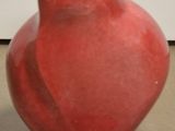 un vase rouge accroché au mur, à côté d'un mur blanc