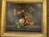 tableau représentant une nature morte aux fruits, dans un cadre doré, posé sur un tissu blanc