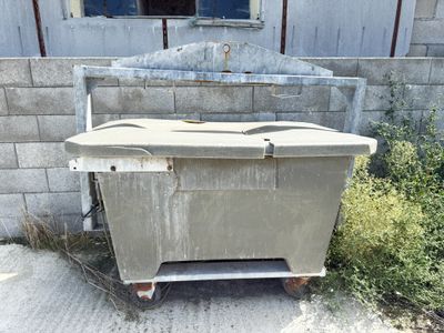 a dirty box sitting outside of a building next to a bush
