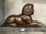 une statue en bronze représentant un lion couché sur un socle en marbre