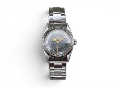 une image représentant une montre montée sur un bracelet en métal, posée sur une surface blanche