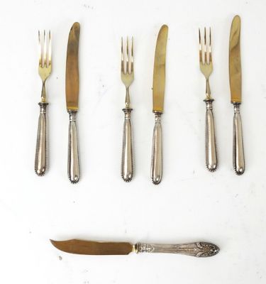 quatre fourchettes, un couteau et un autre couteau posés sur une surface blanche