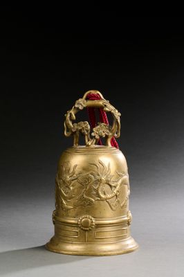 une clochette dorée richement décorée, à laquelle est accroché un ruban rouge au niveau du col