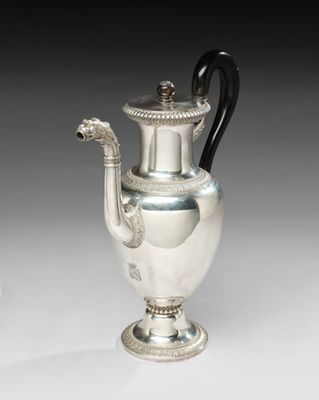 une cafetière ancienne en argent avec une poignée noire sur une surface blanche