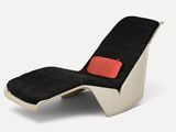 une photo d'une chaise longue en noir et blanc avec un coussin rouge