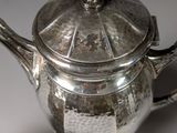 a silver teapot with a lid and a spoon next to it