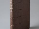 un livre en cuir marron avec des bordures dorées sur fond gris
