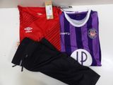 un maillot de foot violet et rouge et un pantalon noir posés sur une table blanche