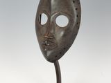 un masque en bronze posé sur un socle, sur fond blanc