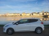 the white car is parked by the river in front of the city