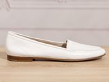 the white loafer is on a wooden table with a pink wall in the background