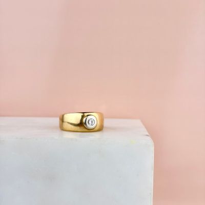 une bague en or sertie d'un diamant repose sur un bloc de marbre