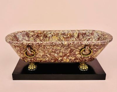 a marble bathtub on a black stand with gold handles