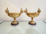 two gold vases on a glass table with a white wall in the background