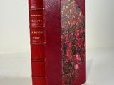 an old book with a red cover sitting on top of a white table