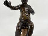 statue en bronze représentant un garçon assis sur un rocher, les mains tendues