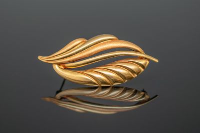 un gros plan d'une broche en feuille d'or posée sur une surface réfléchissante