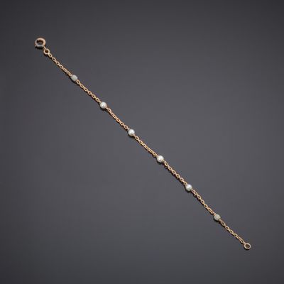 a gold bracelet with pearls and a chain on a gray background