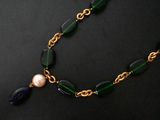 a close up of a necklace with a pearl and green glass beads