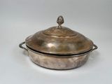 une cocotte ancienne en métal argenté avec un couvercle, posée sur un plan de travail blanc
