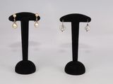deux paires de boucles d'oreilles posées sur un présentoir noir, sur fond blanc