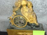 a gold clock with a woman sitting on top of it