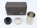 a close up of a metal cup and a black box on a white surface