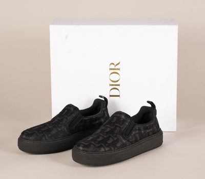 une paire de baskets noires sans lacets devant une boîte blanche