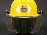 yellow fireman ' s helmet on a black stand against a gray background