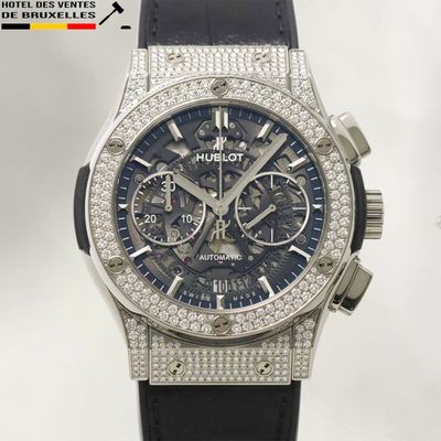 La montre est en acier inoxydable et est dotée d'un bracelet en cuir noir.