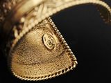 close up of a gold cuff with a chain around it on a black surface