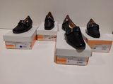 Quatre paires de chaussures noires sont exposées dans une vitrine.
