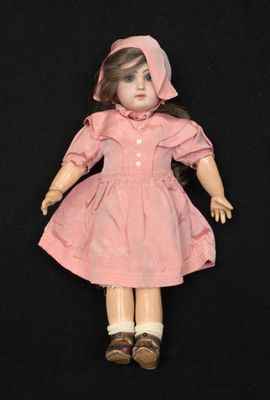 une poupée à l'ancienne, vêtue d'une robe rose et d'un bonnet, sur fond noir