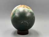 une image représentant un vase vert et orange posé sur un socle en bois