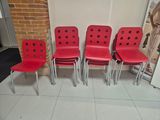 four red chairs are lined up in a row in front of a brick wall