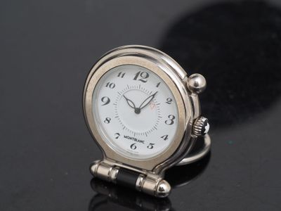 une petite horloge argentée posée sur une surface noire