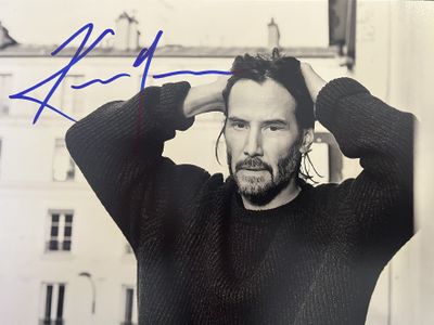 un homme barbu, vêtu d'un pull, posant devant un immeuble