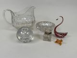 un pichet en verre, un saladier en verre et une figurine de cygne en verre posés sur une surface blanche