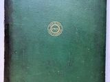 an old book with a green cover sitting on top of a white table