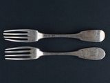 two forks are sitting side by side on a black surface