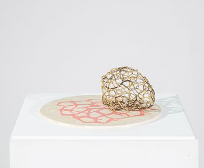 sculpture représentant une boule dorée posée sur un socle blanc orné d'un motif rouge