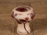 a white vase with a red flower on it on a wooden floor