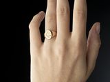 someone is holding their hand up with a gold ring on it