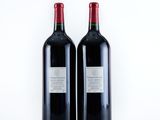 two bottles of red wine sitting next to each other on a white surface